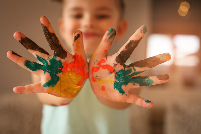 imagem de uma criança brincando com as mãos pintadas de várias cores