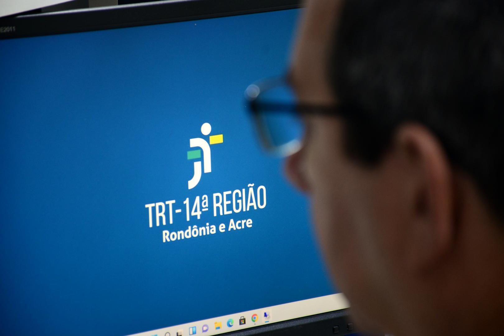 A imagem mostra o perfil do rosto de um homem olhando para a tela de um computador com a logo do TRT-14