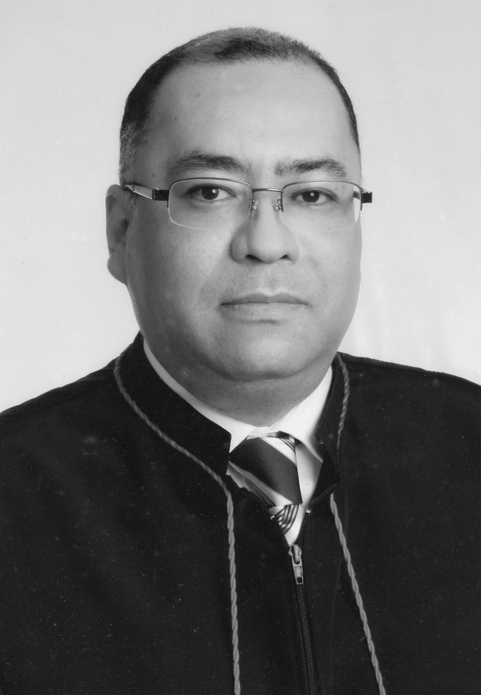 Fotografia em preto e branco, homem pardo, usando óculos, cabelo negro, usando toga.