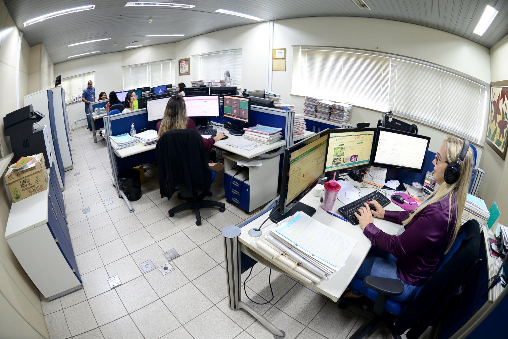 A foto mostra a sala da Secretaria de Precatórios, e alguns servidores trabalhando.