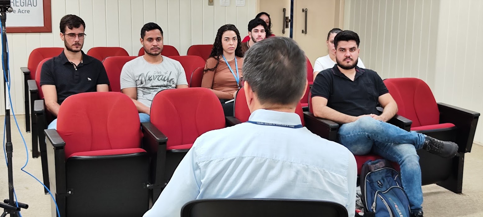 A foto mostra um homem de frente para um grupo de jovens dentro de um auditório.