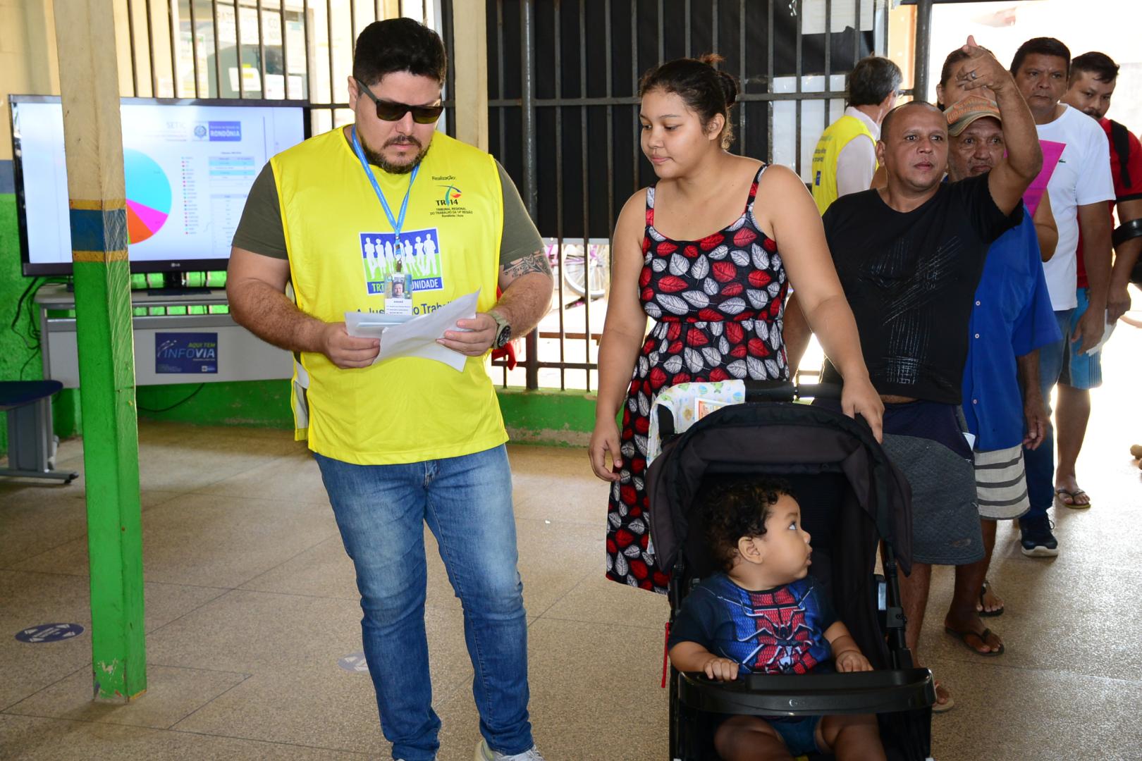 A imagem mostra um voluntário da ação orientando uma mãe que esta com o filho no carrinho