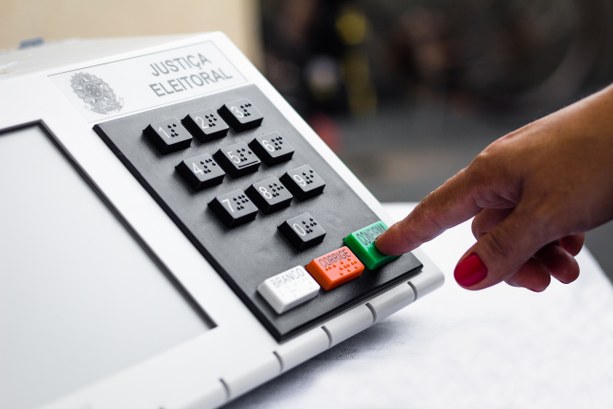 A foto mostra uma mão feminina apertando a tecla confirma da urna eletrônica