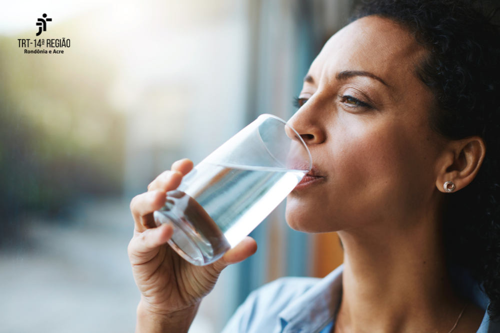 Foto de uma mulher bebendo um copo de água em um copo de vidro.