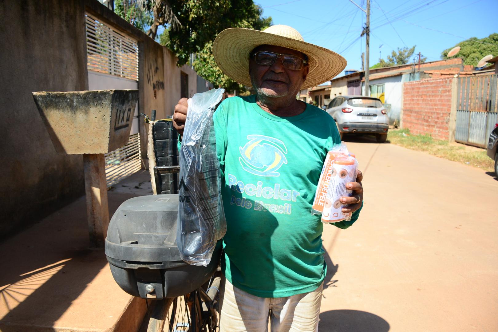 Foto de um catador com as botas e o protetor solar nas mãos.