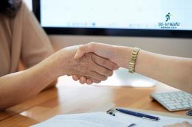 Duas pessoas apertam as mãos sobre uma mesa com documentos e caneta, em um ambiente que sugere a formalização de um acordo.